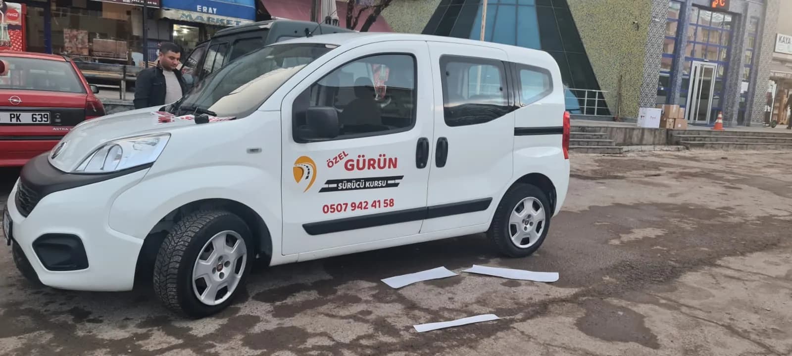 Yan kapısında Özel Gürün Sürücü Kursu logosu ve telefon numarası bulunan beyaz, hafif ticari tipte eğitim aracı