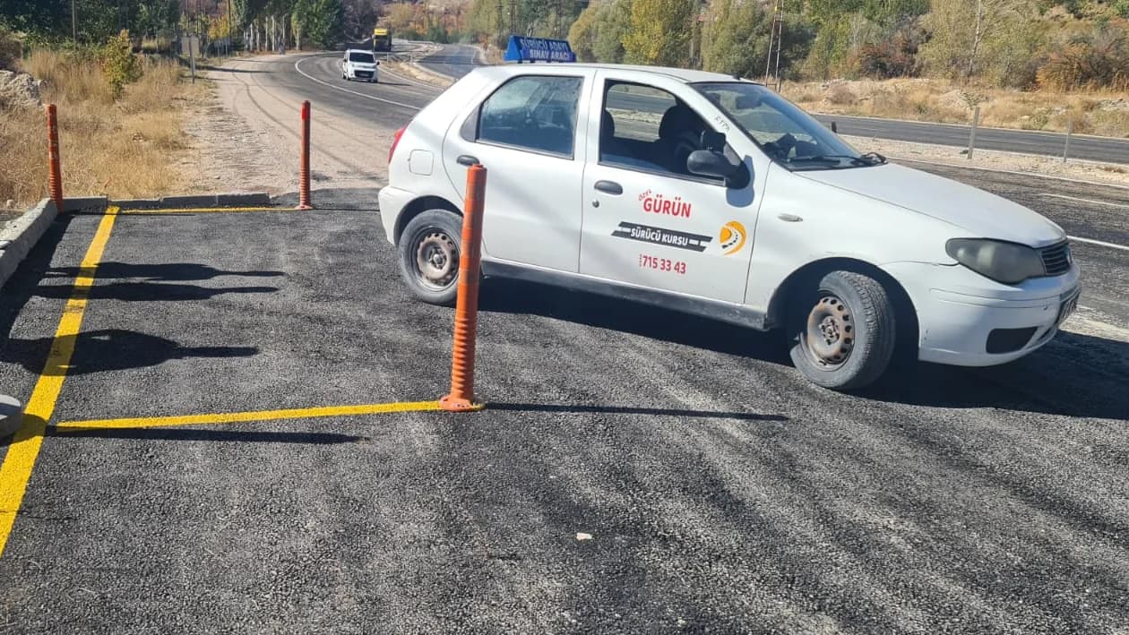 Direksiyon sahasında sarı çizgilerle ayrılmış park alanı ve turuncu dubaların yanında dönen eğitim aracı