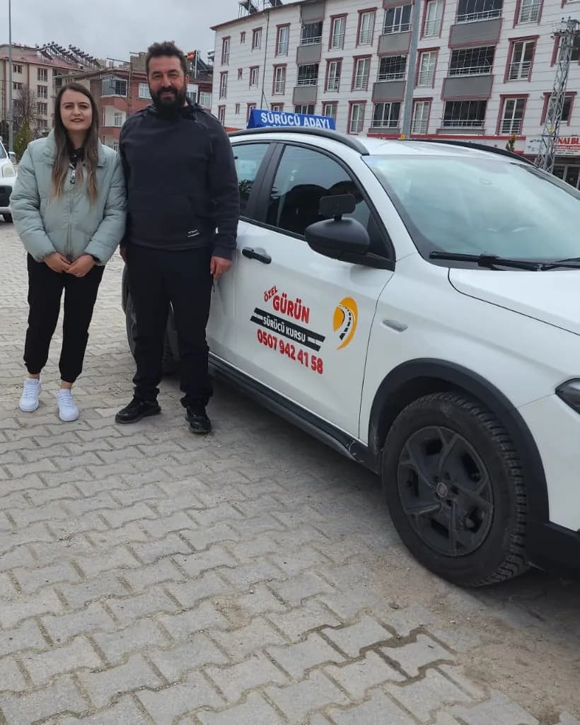 Kapısında Özel Gürün Sürücü Kursu logosu bulunan eğitim aracının yanında yan yana duran bir kadın ve bir erkek
